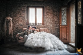 At Villa San Biagio in Mason Vicentino, Italy, a portrait titled "Whispers on Velvet" captures an intimate scene with the groom and bride seated on a cozy couch by the window, her huge dress billowing around her.
